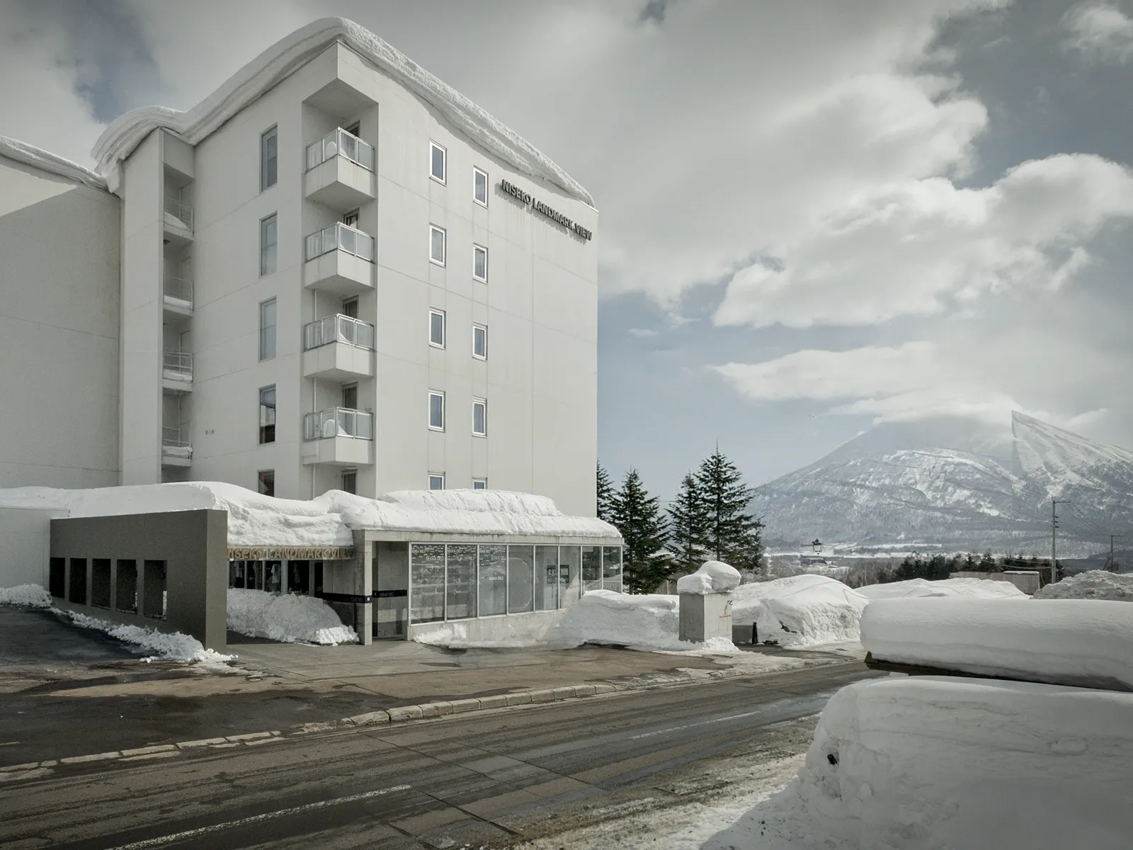 White multi-storey hotel building with snow-covered grounds and mountain views in background.
